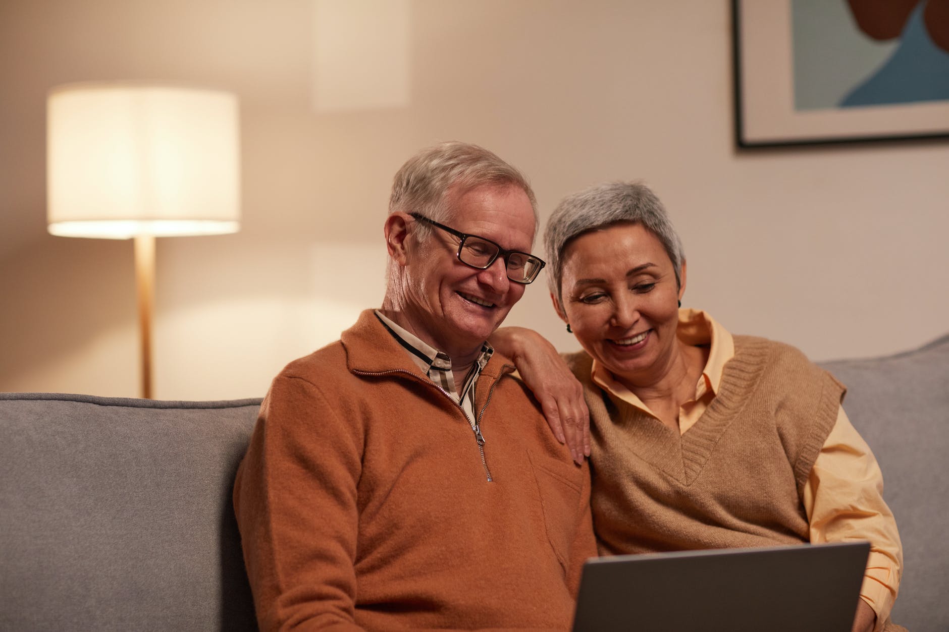 man and woman sitting on sofa while looking at a laptop